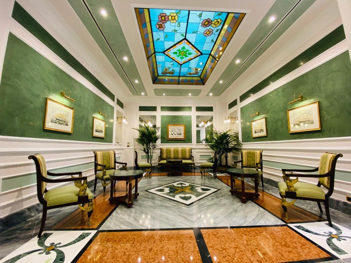Hotel Bristol Palace Génova Exterior foto The photo shows a well-decorated interior space, likely a lobby or reception area. The walls are painted a soft green, and the ceiling features a colorful stained glass design with geometric patterns. 

There are several elegant furnishings, includin