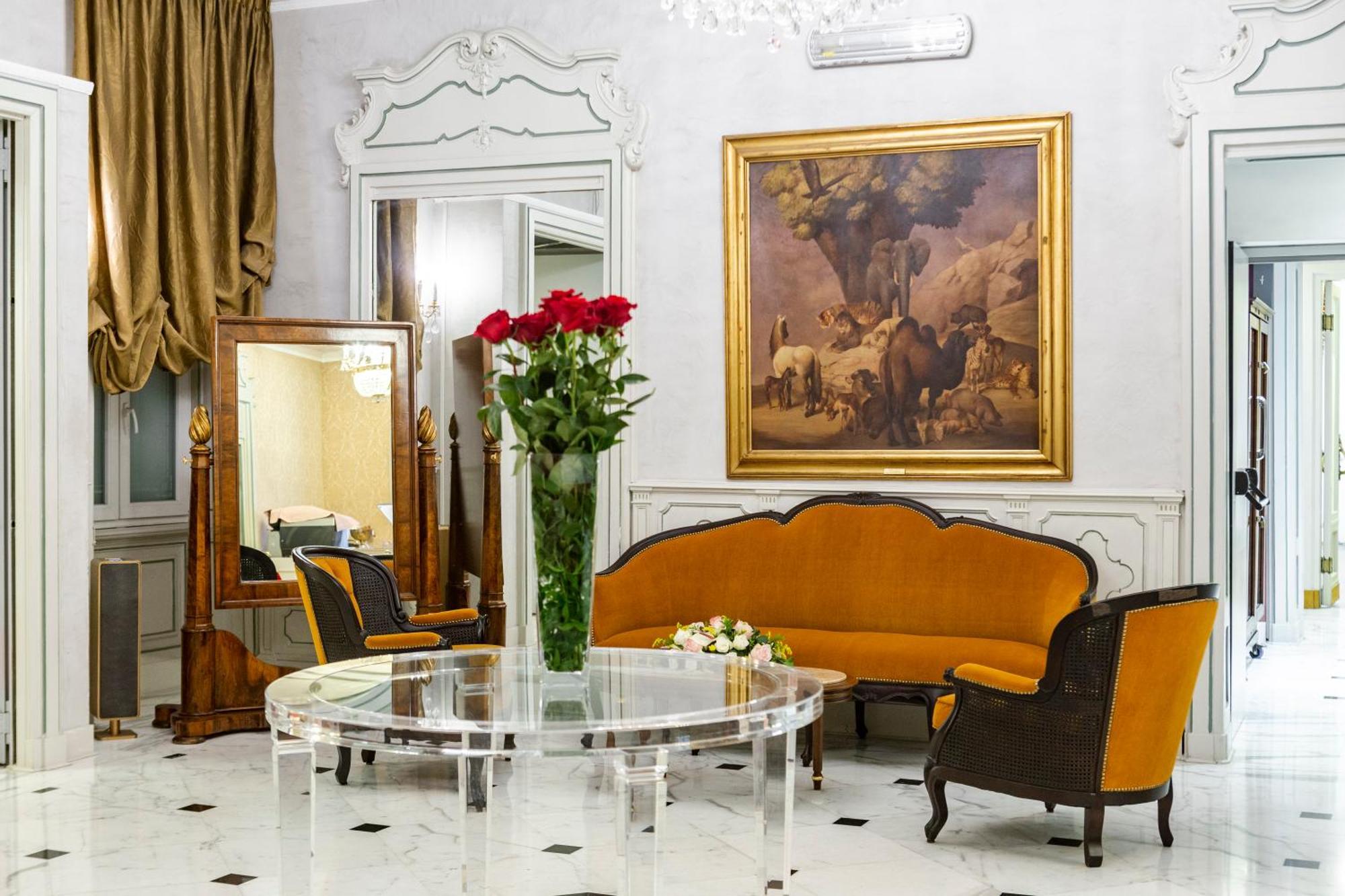 Hotel Bristol Palace Génova Exterior foto The photo displays an elegant interior setting, likely a living room or reception area. Key features include:

- A round glass table placed in the center.
- An orange upholstered sofa with a curved design, complemented by matching chairs with dark wo