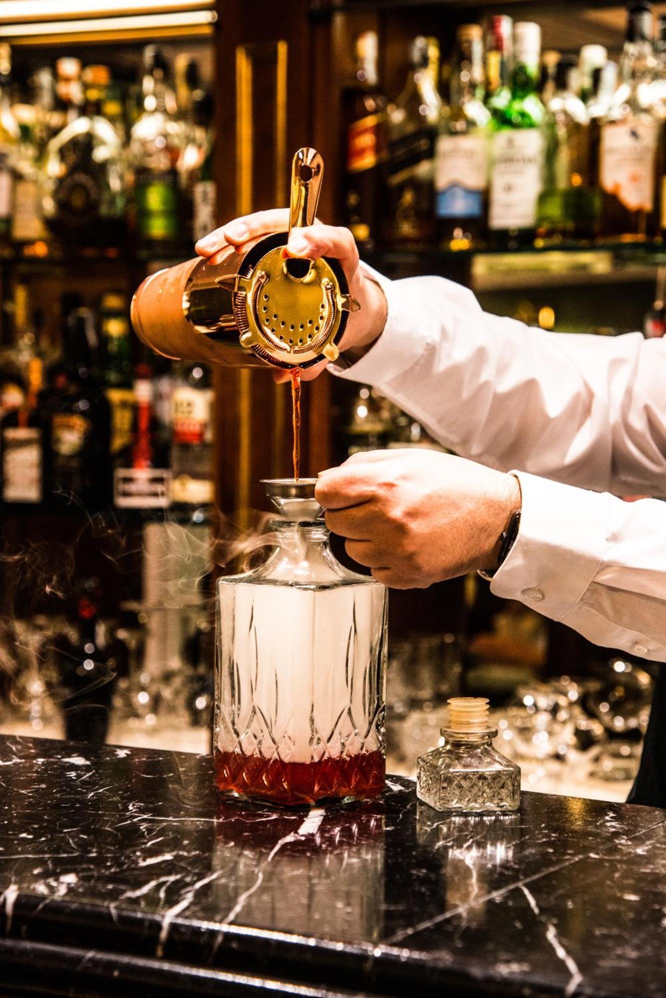 Hotel Bristol Palace Génova Exterior foto The photo shows a bartender pouring a liquid from a cocktail shaker into a glass bottle or decanter. The bartender is holding a strainer over the bottle to catch any solid particles, ensuring a smooth pour. The background displays various bottles of 