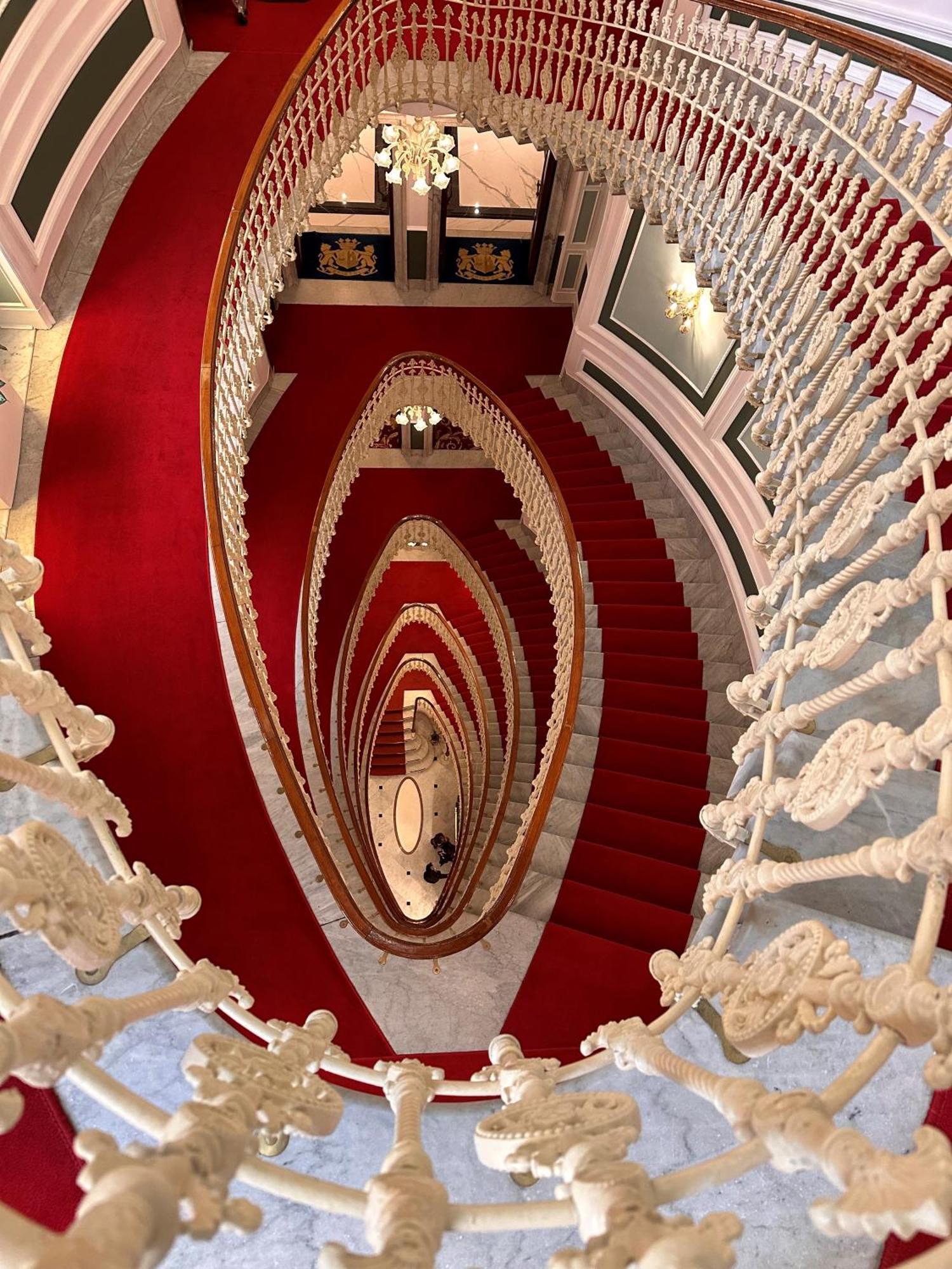 Hotel Bristol Palace Génova Exterior foto The photo depicts a spiraling staircase viewed from above. The staircase features ornate, white railings and a striking red carpet that runs down the steps. The spiral design creates a visual effect of depth, leading the eye downwards. The surroundin