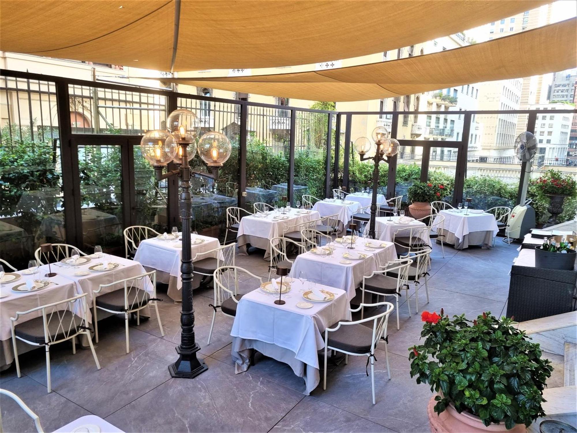 Hotel Bristol Palace Génova Exterior foto The photo shows an outdoor dining area of a restaurant. There are several neatly arranged tables covered with white tablecloths, set with plates and utensils. The space is adorned with decorative lanterns on tall stands, providing a cozy atmosphere. 