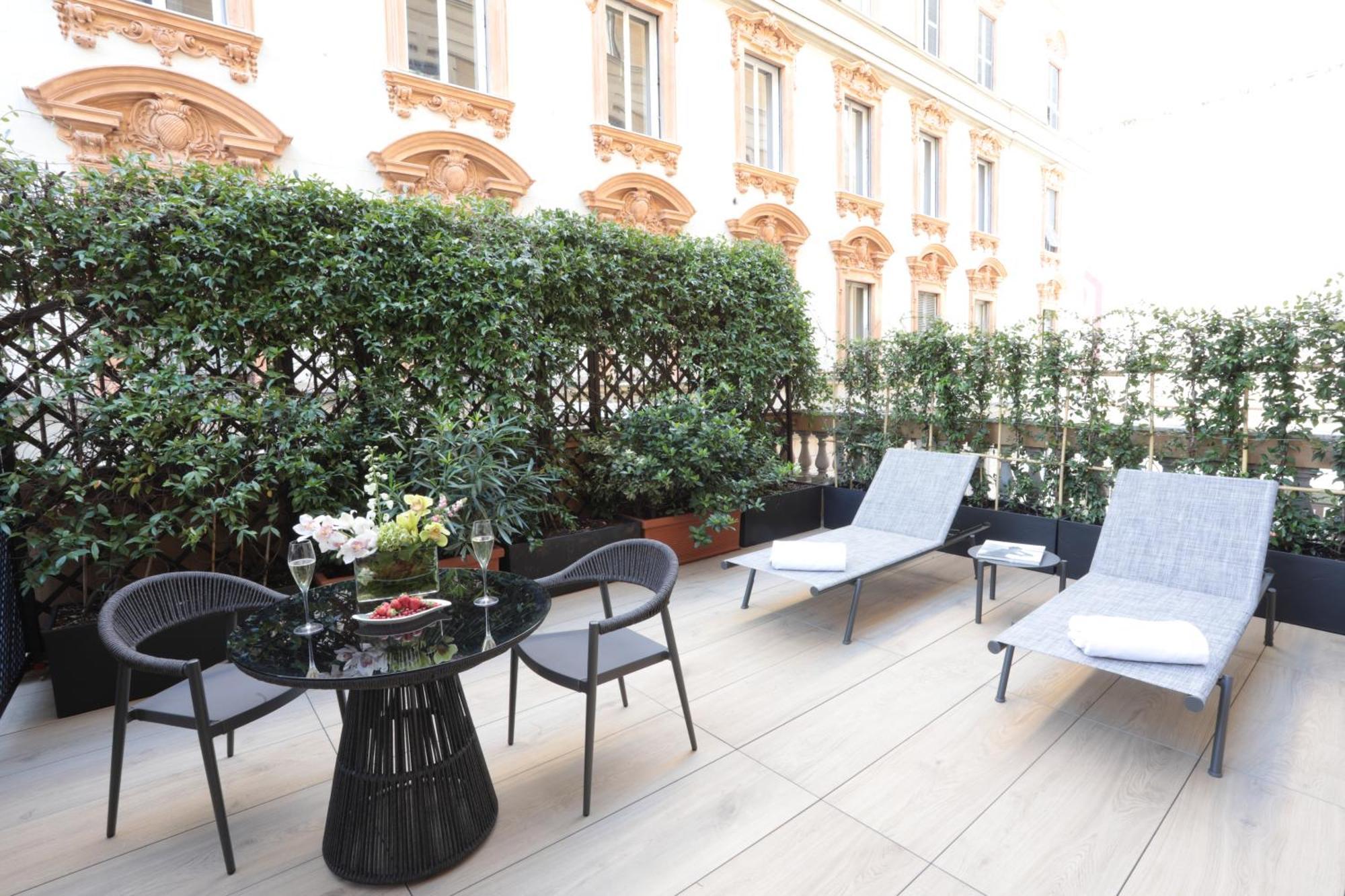 Hotel Bristol Palace Génova Habitación foto The photo shows a stylish outdoor terrace area. It features a round black table with a decorative arrangement of flowers and two glasses, possibly for beverages. Surrounding the table are four black chairs. There are also two gray lounge chairs posit